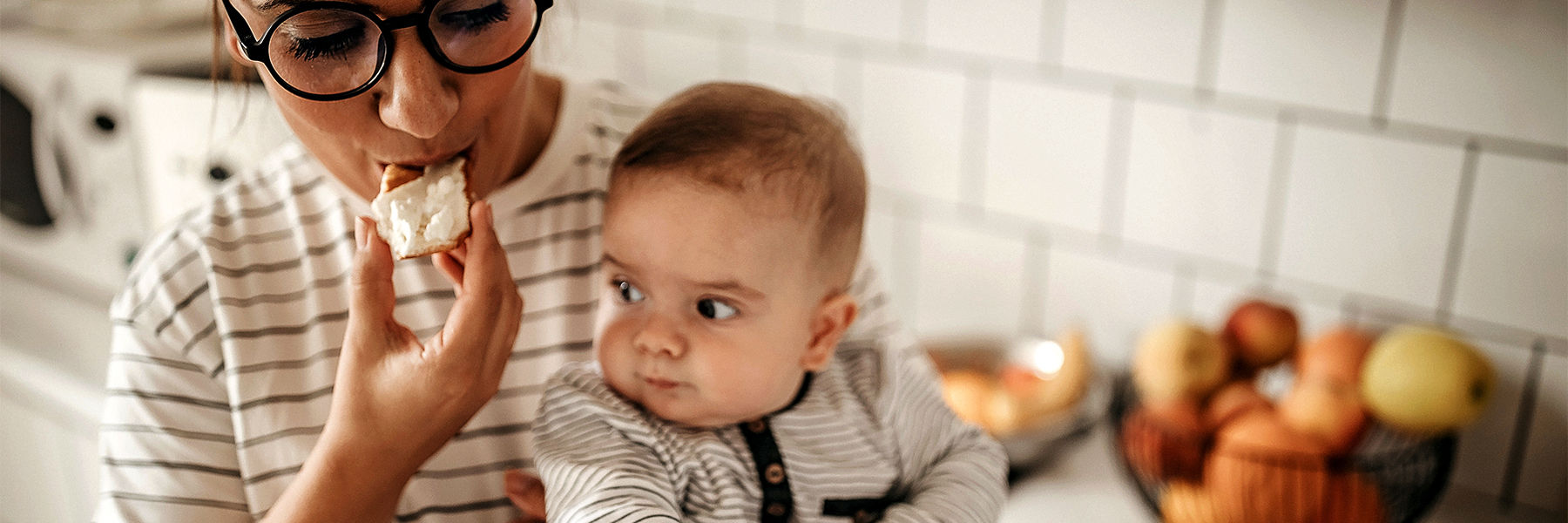 Mother eating a snack whilst holding baby